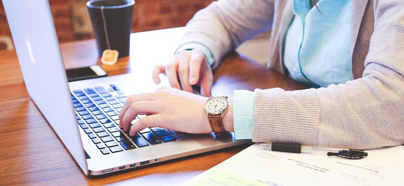 Person typing on a laptop, creating content for inbound marketing strategies, with documents and a coffee cup nearby.
