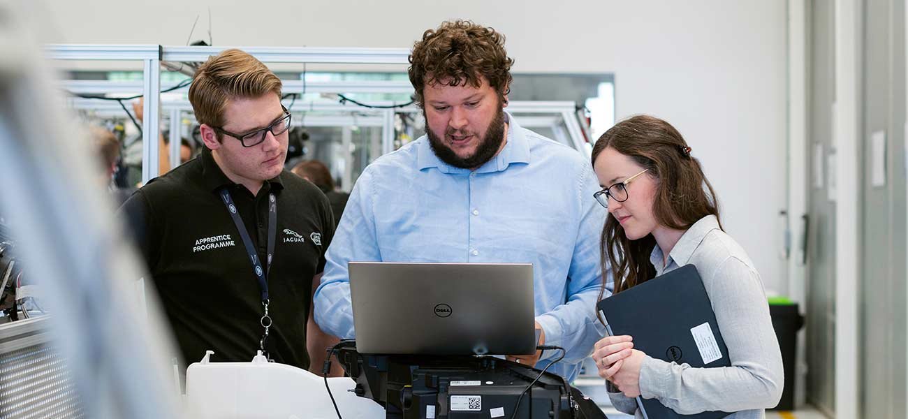 Three professionals discussing email marketing strategies while reviewing data on a laptop, emphasizing the importance of A/B testing and interactive elements in improving click-through rates.