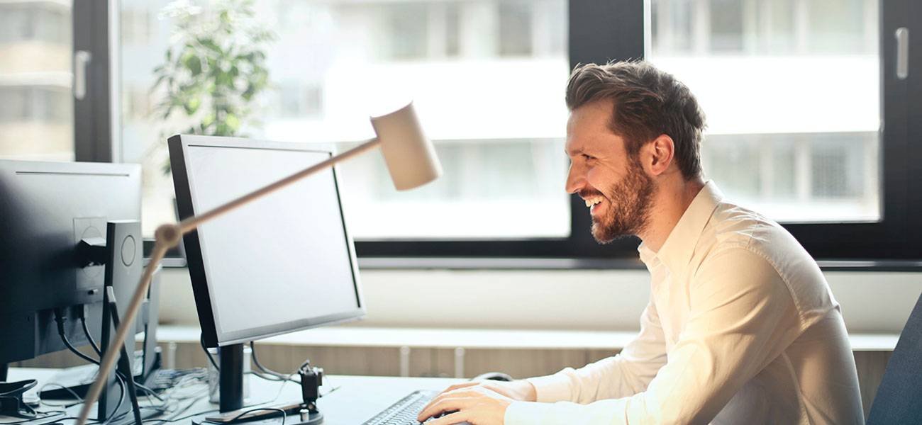 Man smiling while working at a desk with two computer monitors, illustrating the importance of engagement in email marketing strategies.