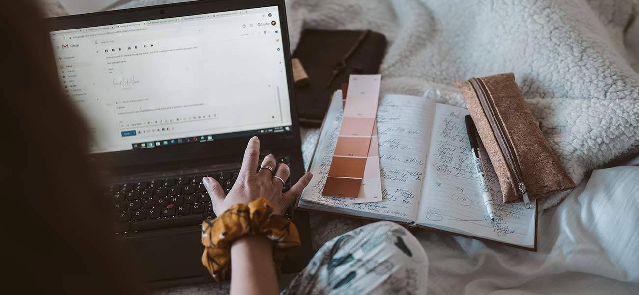 Person typing on a laptop, drafting an email, with a notebook and color swatches nearby, illustrating the importance of timing and content in email marketing campaigns.
