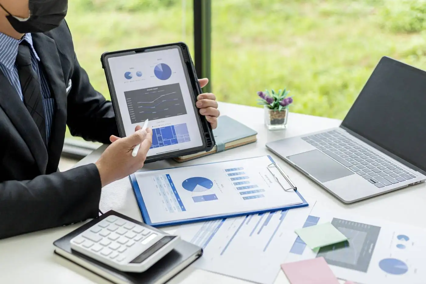 Business professional analyzing data on a tablet, surrounded by financial reports, a calculator, and a laptop, emphasizing automation and efficiency in business processes.