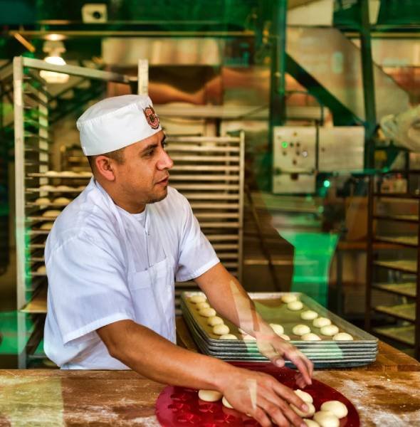 Baker shaping dough in a bakery, showcasing hands-on preparation for custom orders, reflecting the warm, welcoming vibe of a bakery environment.
