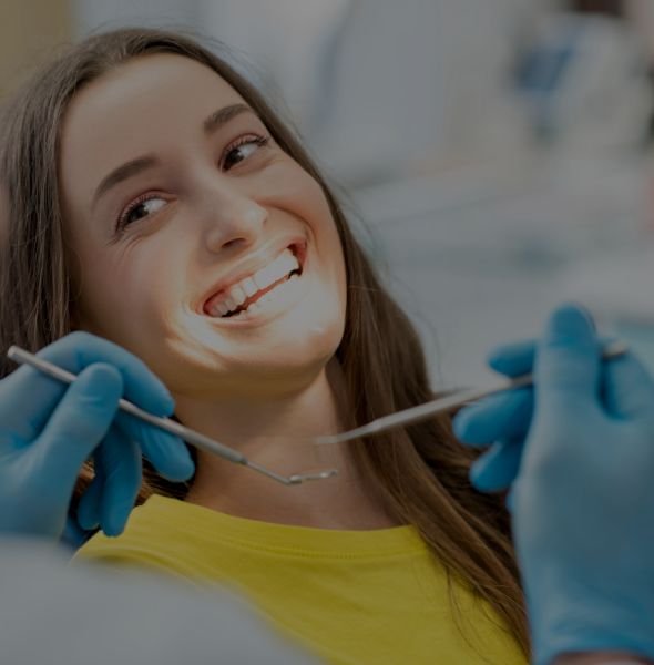 Smiling patient in dental office receiving care, with dentist tools and gloved hands visible, highlighting a friendly and professional dental experience. Smiling patient in dental office receiving care, with dentist tools and gloved hands visible, highlighting a friendly and professional dental experience.